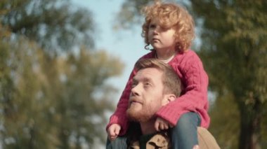 Baba oğlunu omuzlarına alıyor, çocukla konuşuyor, yakın aile ilişkisi yaşıyor.