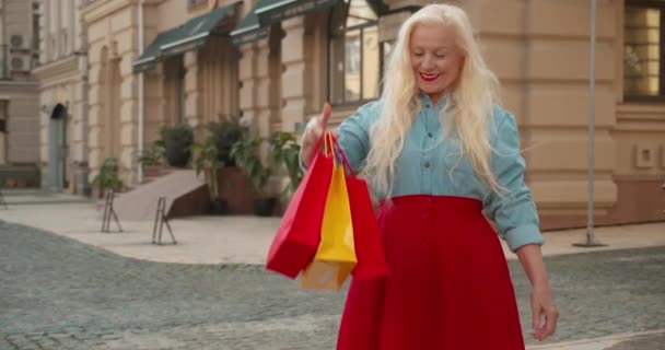 Senior mujer rubia con estilo sosteniendo bolsas de compras, sonriendo, regocijo descuento — Vídeo de stock