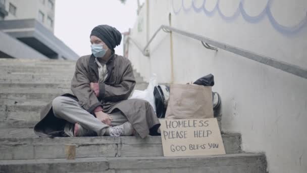 Pengemis kotor dengan topeng pelindung batuk, merasa dingin, hidup di jalanan — Stok Video