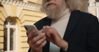 Sakallı yaşlı adam akıllı telefonu kaydırıyor ve gülüyor, internette sohbet ediyor, mobil uygulama