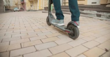 Spor ayakkabılı bir adam şehirde elektrikli scooter kullanıyor, ayakları yakın çekim eko ulaşımı