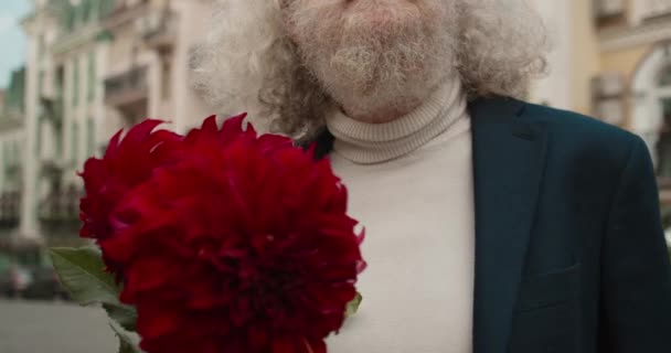 Ideges szakállas idős férfi vörös virágokkal várja a házastársát, ellenőrzi az időt. — Stock videók