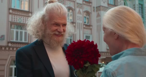 Retraité barbu souriant présentant des fleurs rouges à la femme blonde aimante, date — Video