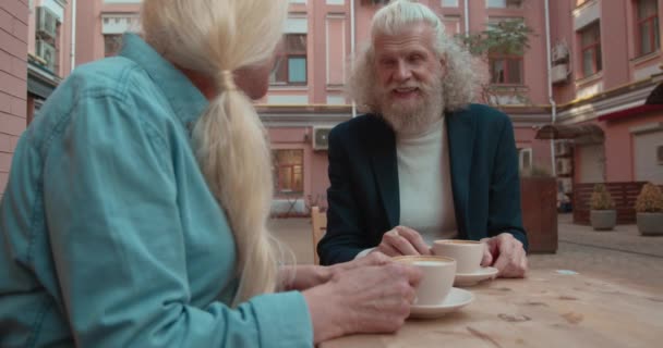 トレンディなひげそり老人チャットブロンド女性とともにコーヒーショップテラス,日付 — ストック動画