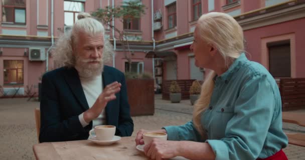 Pareja mayor consciente de la moda discutiendo en la terraza de la cafetería durante el descanso del café — Vídeo de stock