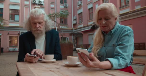 Beledigd oud paar scrollen smartphones in outdoor cafe, relatie probleem — Stockvideo