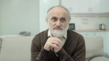 Endişeli emekliler üzgün hissediyor, evdeki kanepede oturuyor, hayal kırıklığına uğruyor.