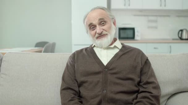 Добрый пожилой мужчина улыбается в камеру, позитивный здоровый пенсионер расслабляется дома — стоковое видео