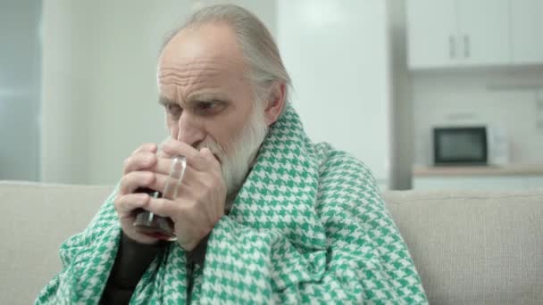 Hombre maduro enfermo que bebe té caliente, cubierto con manta, síntomas de gripe, virus — Vídeo de stock