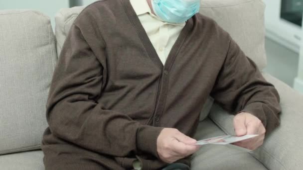 Больной пожилой человек в защитной маске, пропавшие внуки, смотря на фотографии — стоковое видео