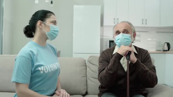 Старик в защитной маске разговаривает с волонтером, социальной помощью, карантином — стоковое видео