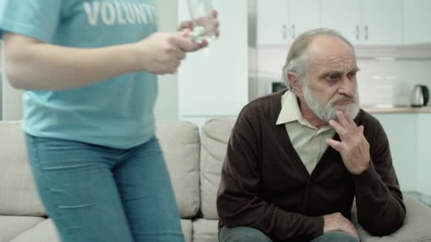 Maatschappelijk werker die pillen en glas water aanbiedt aan ontevreden oude man, help — Stockvideo