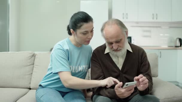 Trabajador social explicando anciano cómo utilizar el teléfono inteligente, tecnología moderna, ayuda — Vídeos de Stock