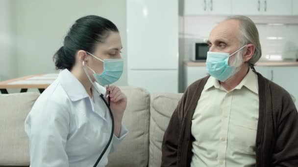 Kvinnlig läkare i mask kontrollerar patientens lungor, med hjälp av stetoskop, hälsovård — Stockvideo