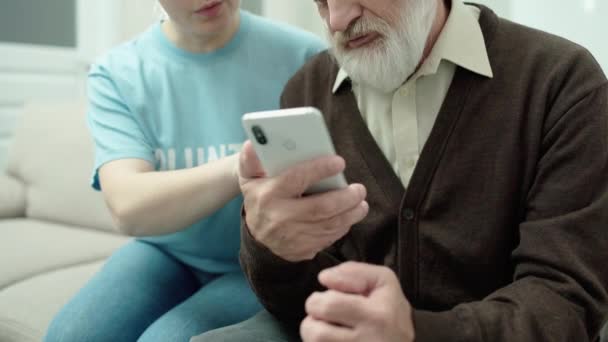 Szczęśliwy emeryt uczy się używać smartfona, wolontariat pomaga staremu mężczyźnie, organizacja charytatywna — Wideo stockowe