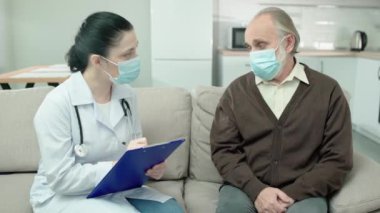 Koruyucu maske takan bir klinik çalışanı tanı yazıyor, kıdemli hastalarla konuşuyor.