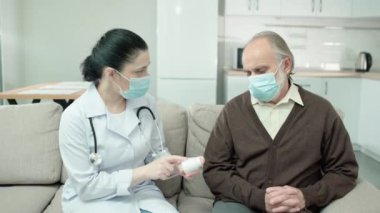 Maskeli hasta yaşlı bir adam doktorun elinden ilaç şişesi alıyor.