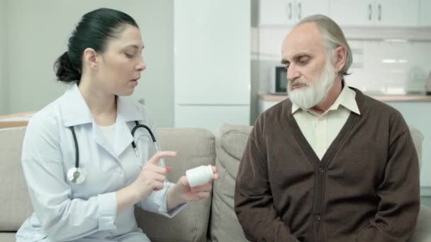 Joven terapeuta que prescribe tratamiento para el hombre anciano, sosteniendo frascos de pastillas, salud — Vídeo de stock