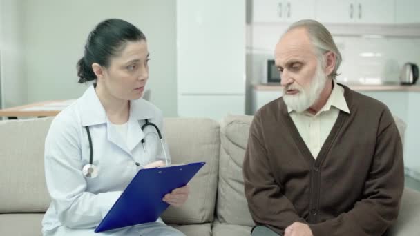 Терапевт выписывает симптомы, разговаривает со старшим пациентом дома, рецепт — стоковое видео
