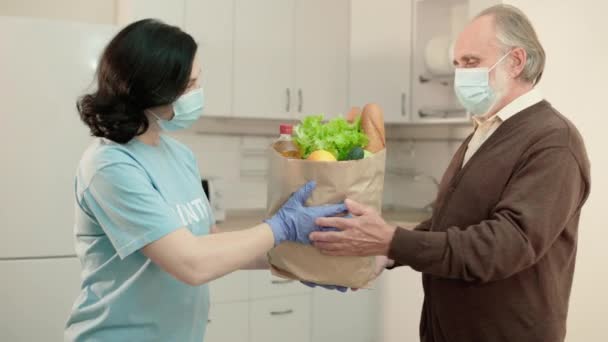 Social worker in protective mask giving groceries to aged pensioner, charity — Stock Video