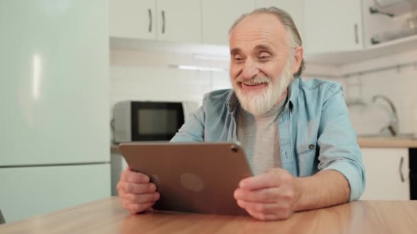 Hombre jubilado alegre hablando con la familia, utilizando la aplicación de la tableta en casa, la tecnología — Vídeos de Stock