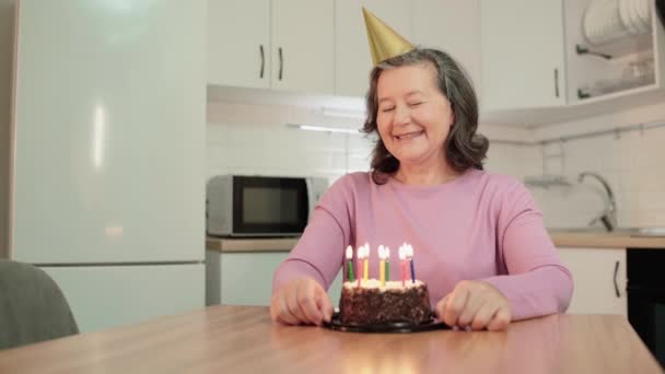 Opgewonden senior vrouw blaast kaarsen, het maken van wens op verjaardagsfeestje, plezier — Stockvideo