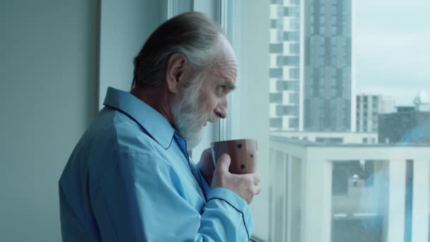 Uomo in pensione sconvolto lamentarsi del tempo, bere caffè, guardare la finestra — Video Stock