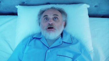 Sinirli yetişkin bir erkek uyanıyor, gürültülü komşuları dinliyor, rahatsız bir uyku çekiyor.