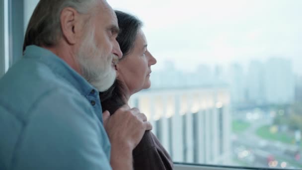 Sad mature couple hugging, standing near the window, life problem, support — Stock Video