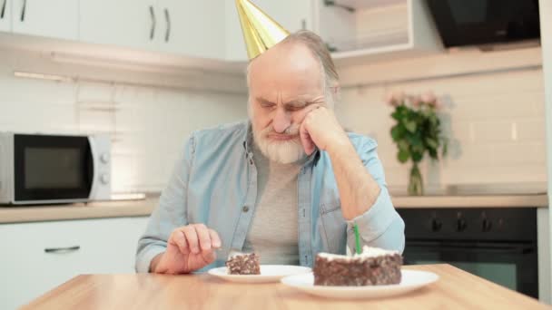 Smutny senior w imprezowym kapeluszu jedzący tort, samotny, urodzinowa depresja — Wideo stockowe