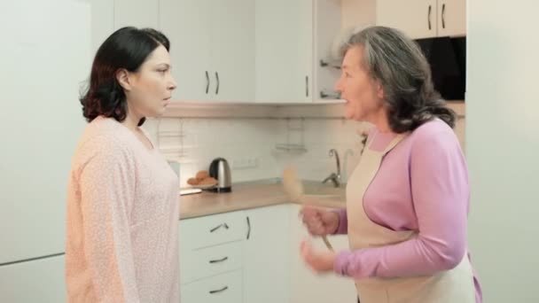Пожилая мать в фартуке спорит с дочерью на кухне, поколения разрыв, конфликт — стоковое видео