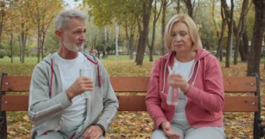 Kadın ve erkek parkta çalıştıktan sonra su içiyor, birlikte bankta oturuyorlar.