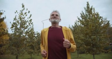 Olgun bir adamın parkta koşması, kablosuz kulaklıkla müzik dinlemesi, sağlık.