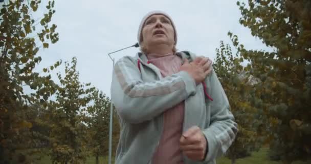 Mujer mayor en deporte sudadera con capucha correr al aire libre, sensación de frío, ropa térmica — Vídeo de stock