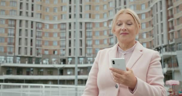 Glückliche blonde Frau genießt Online-Shopping, scrollt am Telefon, zeigt Taschen — Stockvideo
