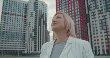 Mutlu kadın emlak müteahhidi iş sonuçlarını beğeniyor, gökdelenlere bakıyor.