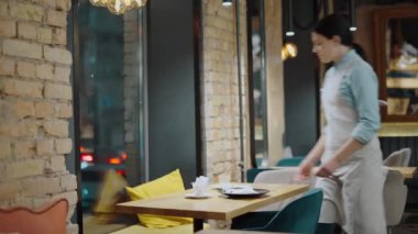 Genç garson kafede masayı temizliyor, kahvecide çalışıyor, servis yapıyor.