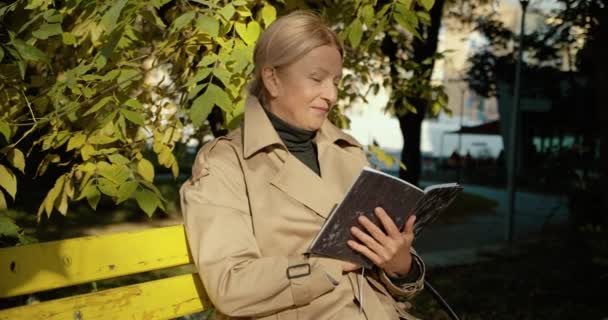 Attrayant livre de lecture féminine senior sur le banc dans le parc, passe-temps préféré, se reposer — Video