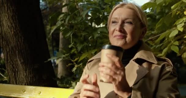 Mujer madura alegre bebiendo café y sonriendo en el parque sintiéndose feliz, buen humor — Vídeos de Stock