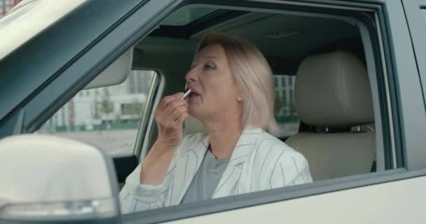 Beautiful senior woman looking in rear view mirror, applying lipstick, smiling — Stock Video