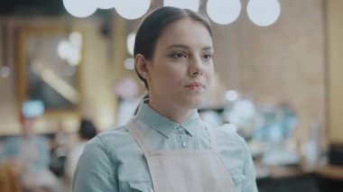 Önlüklü kadın kafe çalışanı kameraya, restoran işine, misafirperverliğe gülümsüyor.