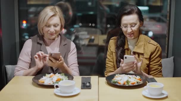 현대 여성들은 스마트폰으로 음식 사진을 찍고 카페에서 저녁을 먹고 있습니다. — 비디오