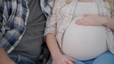 Adam hamile kadının karnına el ele tutuşuyor, bebek tekmeleri hissediyor, mutlu ebeveynlik yapıyor.
