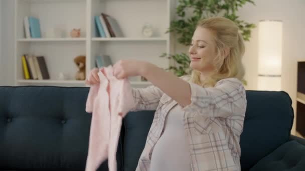 Mujer embarazada feliz sosteniendo traje de recién nacido, la felicidad de la espera, el parto — Vídeo de stock
