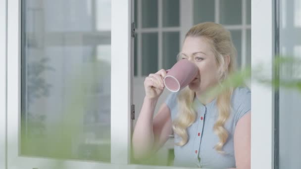 Vrouwelijke kantoormedewerker drinkt koffie bij het raam, ontspant zich tijdens de werkpauze — Stockvideo