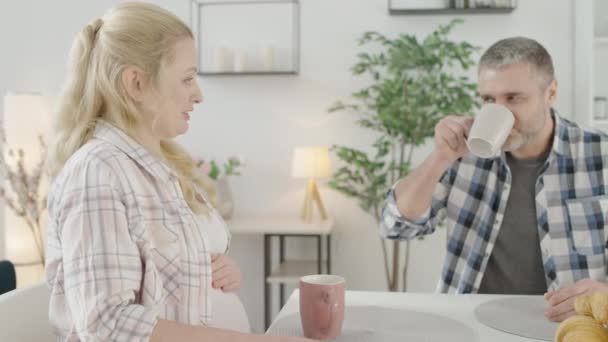 Blij man en zwangere vrouw praten, samen thee drinken in de keuken — Stockvideo