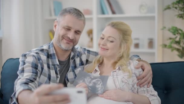 Веселі майбутні батьки беруть селфі, тримаючи ультразвуковий образ, сімейне щастя — стокове відео