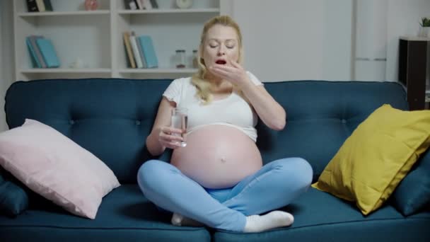 Terhes nő gyógyszert szed, otthon ül a kanapén, terhesgondozás, vitaminok — Stock videók