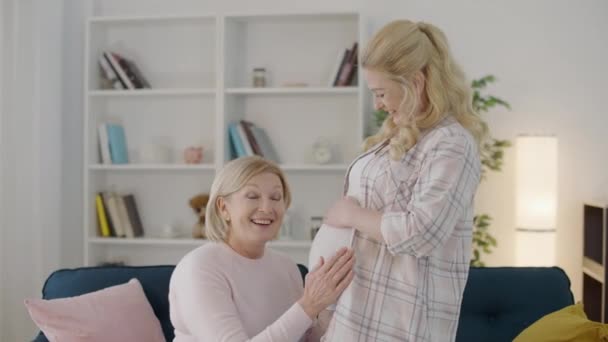 Madre emocionada escuchando el movimiento del bebé en el vientre de la hija embarazada, nacimiento — Vídeo de stock