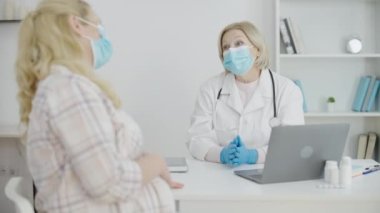 Maskeli ve eldivenli kadın doğum uzmanı hastayla konuşuyor, Coronavirus sırasında hamilelik.